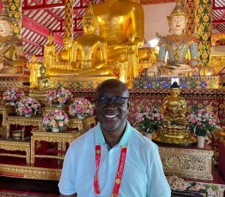 A man in a short-sleeved dress shirt stands smiling in a Buddhist temple.