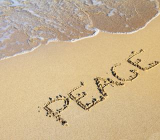 The word "Peace" written in sand on a beach with the shore partially visible.