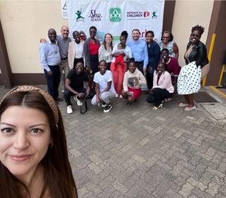 A woman taking a selfie outdoors with a dozen people in the background