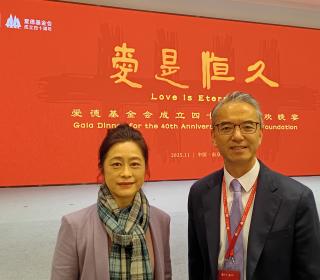 A photo of a man and a woman in front of a red backdrop with yellow Chinese and English phrases written on it