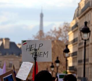 A sign with the words "Help them" is held up at a street protest
