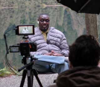 A man being filmed talking on a dock in front of a lake