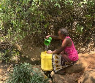 A woman fetching water from a spring with a large plastic jug