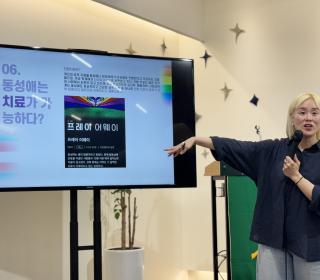 A Korean woman points at a screen with an educational slide on it