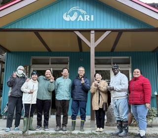 A group of people smiling and holding eggs outside of a farmhouse