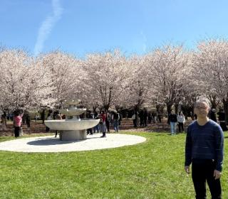 Won Hur smiles in front of a row of cherry blossom trees