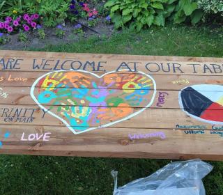 A picnic table with the message "All are welcome at our table" written on it