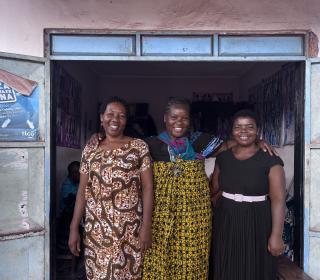 Three African women stand smiling in a doorway