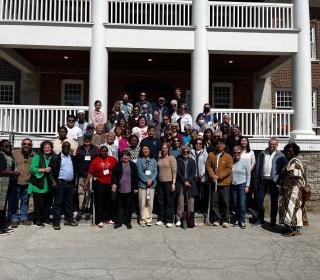 A large group of people stand in front of a brick building with a portico