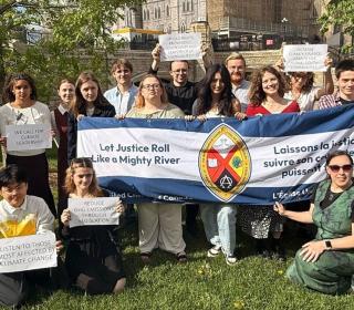 A group of youths hold up signs with slogans calling for climate leadership, as well as a large United Church banner