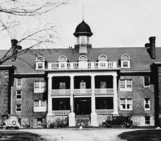 Black and white image of a wide brick building with a portico