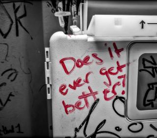Red graffiti with the phrase "does it ever get better" written in a public toilet
