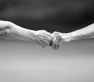 Two older adults reach out to hold each other's hands