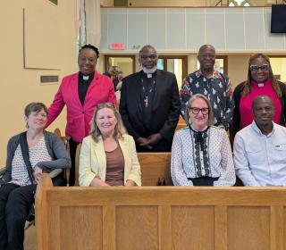 Eight people, five Black and three White, standing and sitting in church pews