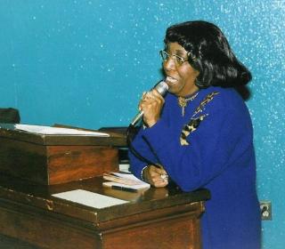 A Black woman in a blue dress speaking into a microphone