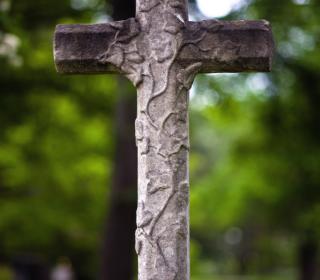 A stone cross standing outside, in front of the a background of green trees.