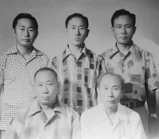 In an aging black and white photo taken sometime around the Korean War, four Korean brothers and their older father face the camera for a formal photo.