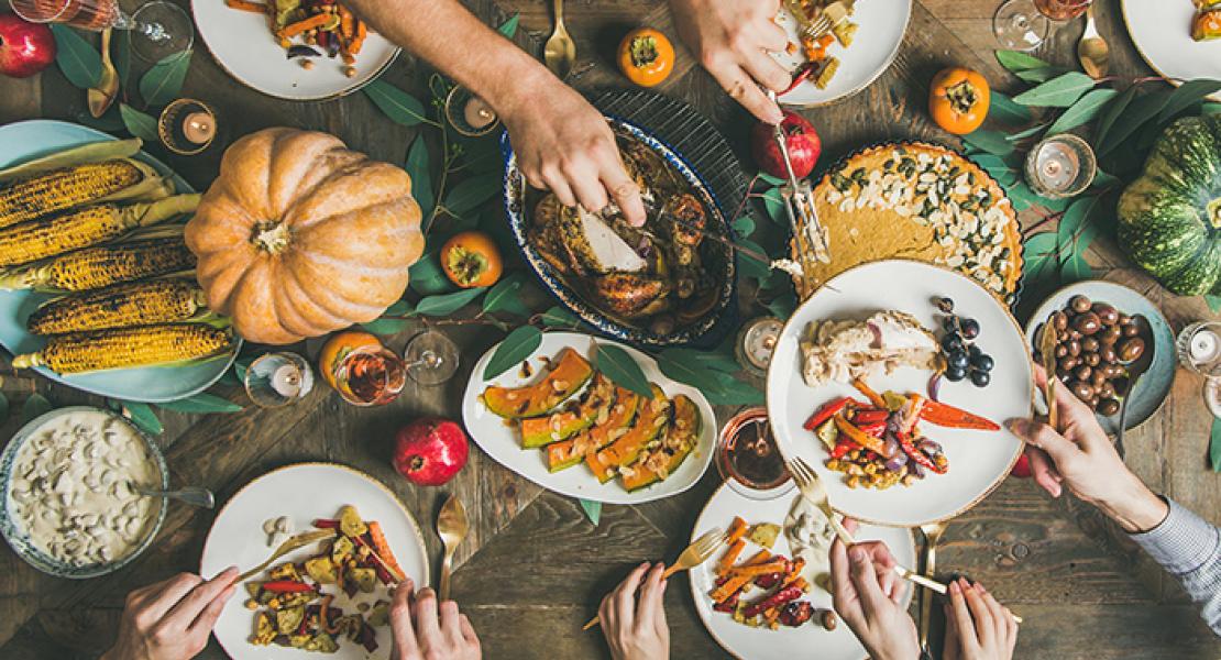 Hands sharing food over a harvest table filled with full plates and seasonal bounty