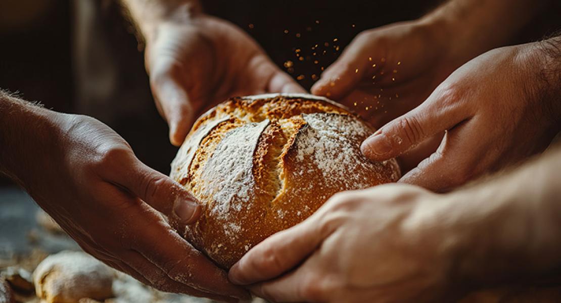 A boule of floured bread being shared with outreached hands