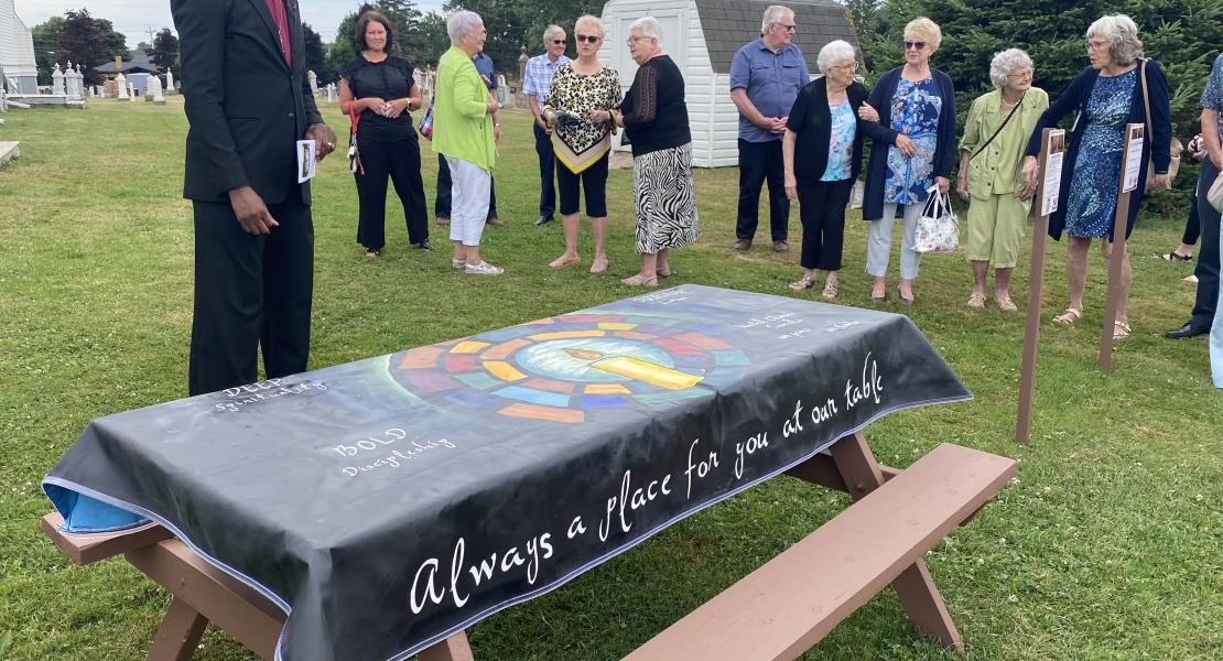 A group of individuals standing in by a picnic table with a United Church covering