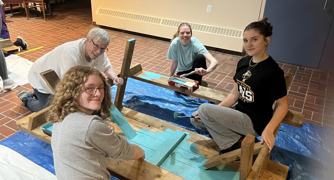 A group of people painting a picnic table turquoise
