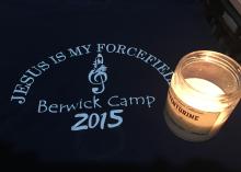 A candle sits upon a black cloth memento, which says "Jesus is my Forcefield, Berwick Camp, 2015.