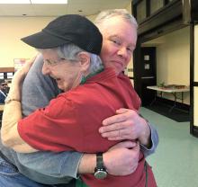 Two participants at 1JustCity, an older White woman and White man, share a hug.