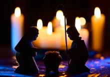 The statues of a Nativity scene are silhouetted by a background of candles.