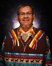 A portrait of the author, an Indigenous man with grey hair and grey beard, and a great smile. Wearing a colourful tradition Indigenous shirt.