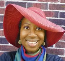 A portrait of author Karlene Cameron, a Black woman in a brilliant large red hat.