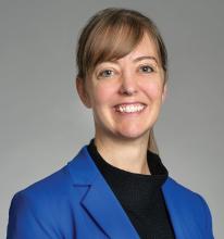 Head shot of Sarah Charters wearing a black turtleneck and royal blue jacket, against a grey backdrop