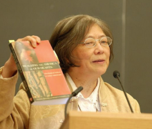 The Rev. Dr. Greer Anne Wenh-In Ng holding a book up during a presentation.