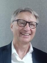 A portrait of Rob Dalgleish, executive director of EDGE Network for Ministry Development. He is a white man with greying hair, large glasses, and an enthusiastic smile. Wearing an open neck white dress shirt and jacket.