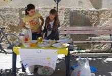Children selling lemonade at a homemade stand outside in the summer.