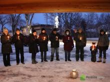 A group of people stand outdoors in a circle with lit candles at dusk