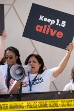 A woman speaking into a megaphone holds up a sign that says Keep 1.5 alive.
