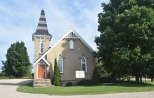 A small white church with a steeple, between two trees.