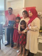 A family of two parents and three young girls holding up a laptop during an online citizenship ceremony.
