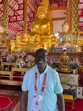 A man in a short-sleeved dress shirt stands smiling in a Buddhist temple.