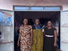 Three African women stand smiling in a doorway