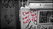 Red graffiti with the phrase "does it ever get better" written in a public toilet