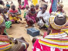 A group of African women sit around a money box in a circle