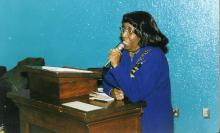 A Black woman in a blue dress speaking into a microphone