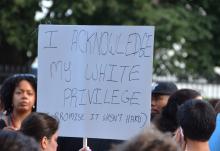 A white woman holds a sign that says, "I acknowledge my white privilege" during a protest.