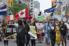 Black Lives Matter supporters march at Toronto Pride 2016, beneath a large Canadian flag and flags representing the Trans movement.