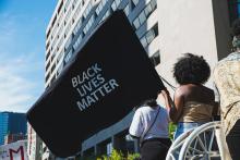 A Black woman seen from behind while holding a large Black Lives Matter flag during a march in downtown Toronto.
