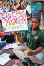 A young person with a sign reading "Stakeholders Not Shareholders."