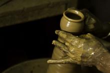 A potter's hands covered with wet clay and shaping a vessel on the pottery wheel in India.