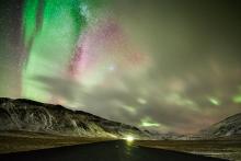 Yellow, green, and pink aurora shines above a isolated road at night.
