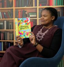 Lenten book editor Alydia Smith, dressed in a long purple dress and detailed necklace, sits in a large comfy to read a copy of the book "Everyday Skeptics."